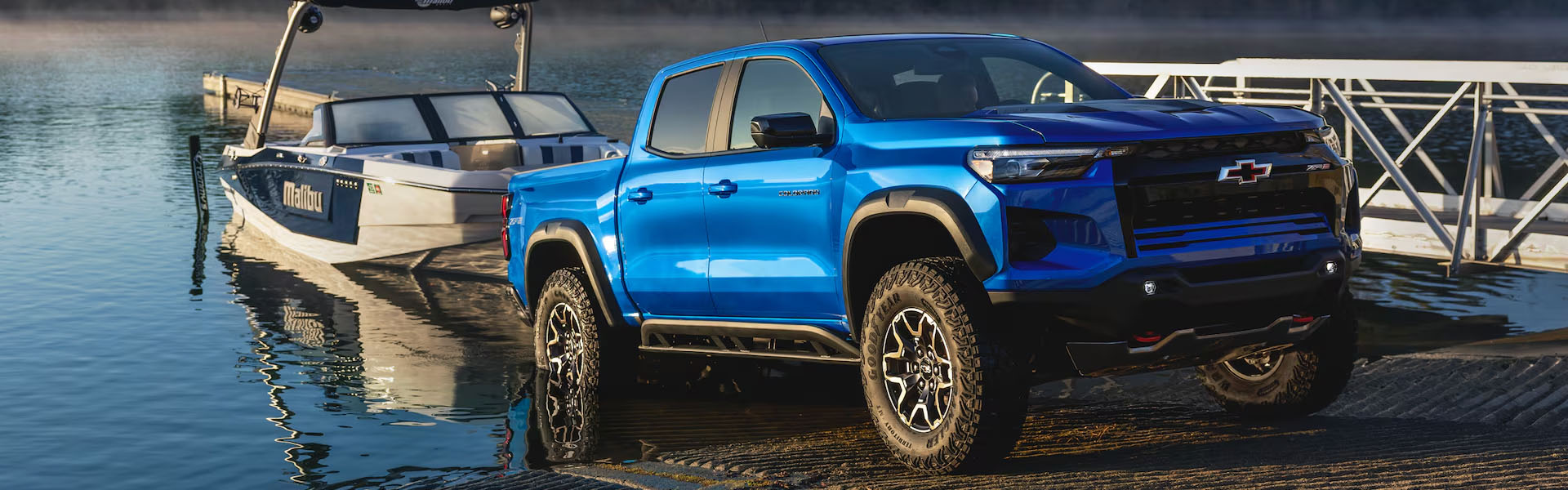 Blue 2026 Chevrolet Colorado parked near a Malibu boat and water.
